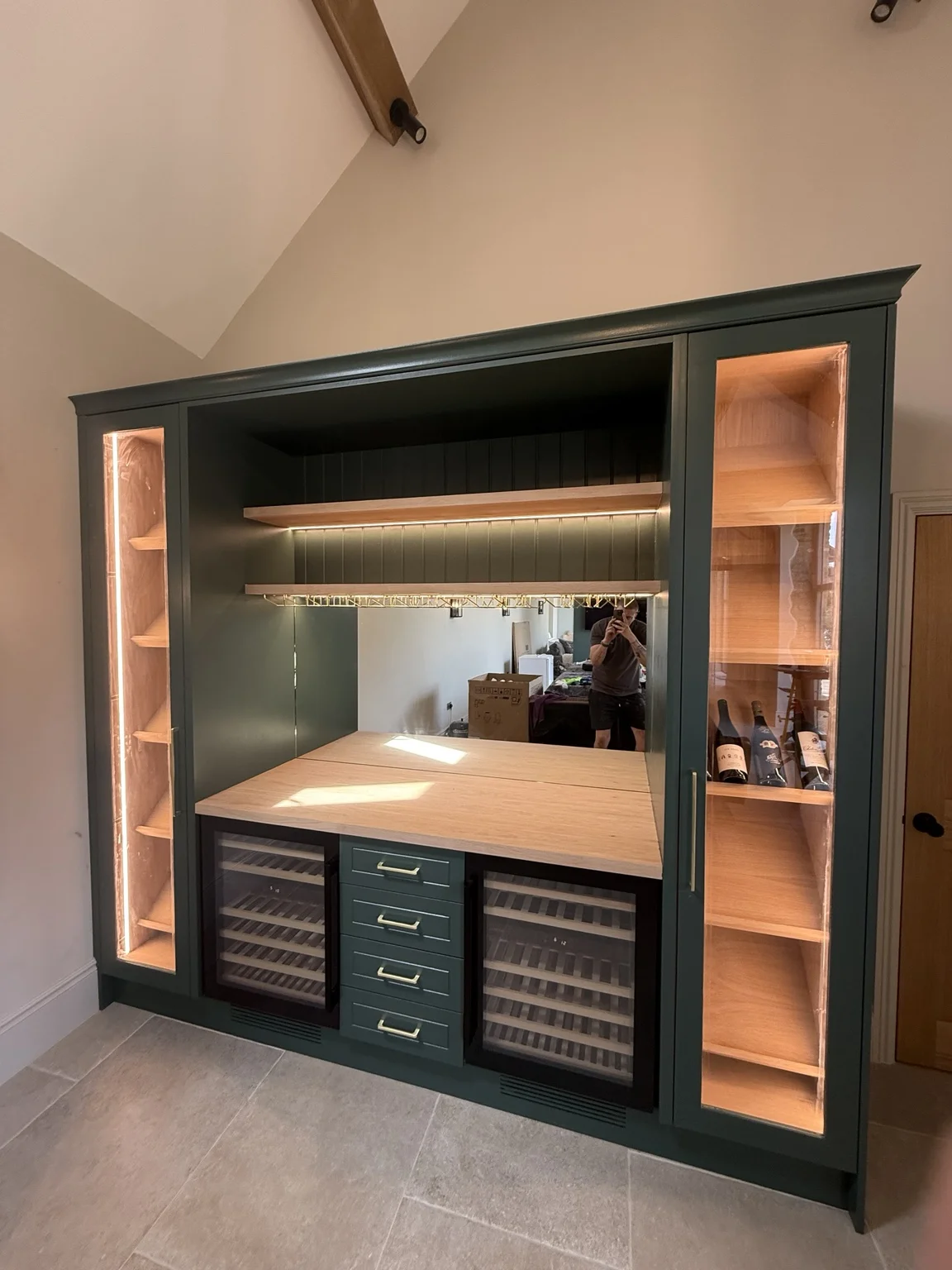 Bespoke dark green home bar with illuminated display cabinets, timber worktop and wine fridges